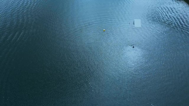 OVERHEAD aerial drone shot of female wake boarding in a cable wakepark on a lake. 4K UHD 60 FPS 