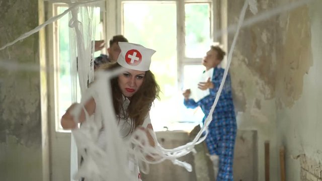 Sexy beautiful young female woman nurse screams and shouts at patients in psychiatric hospital. Psychos catch the doctor in room in mental clinic. Mad crazy people tie up by bandages their doctor