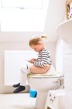Little girl with smartphone sitting on the toilet.