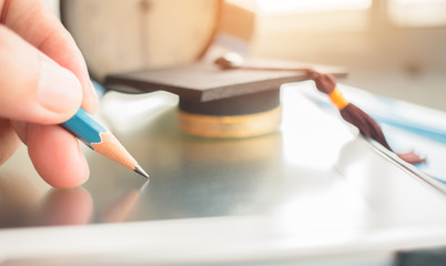 Alarm clock with Graduation cap and optical form of standardized exams or test on touch screen tablet with hand holding blue pencil for examination, Education concept,selective focus,vintage
