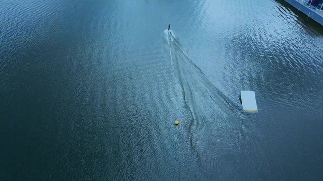 OVERHEAD aerial drone shot of female wake boarding in a cable wakepark on a lake. 4K UHD 60 FPS 