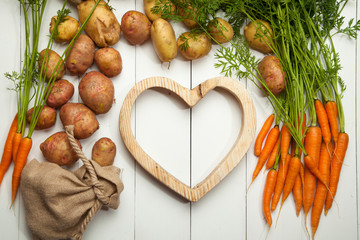 Fresh vegetables, potatoes and carrots against a white wooden background