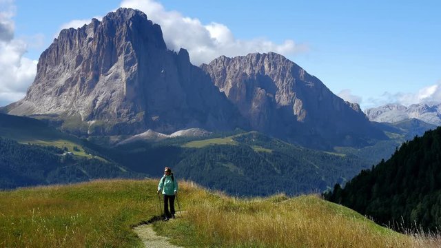 Woman hiking along the path agains a backdrop of Sassolungo mountain peak