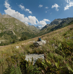 Obraz premium child sits on a stone in the mountains looking at a mountain gorge on a summer day