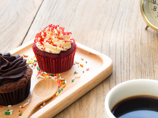 Red and chocolate cupcakes put on a spherical wooden plate. Beside of cupcake have Cactus and white coffee mug.All of it rests on wooden table.