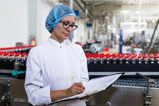 Serious middle age woman quality control worker checking robotic line for bottling and packaging carbonated black juice of soft drink into bottles.
