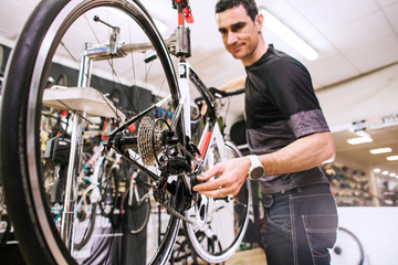 Male master is repairing the bicycle in a special workshop - obrazy, fototapety, plakaty