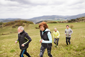 Group of seniors running outside on the green hills.