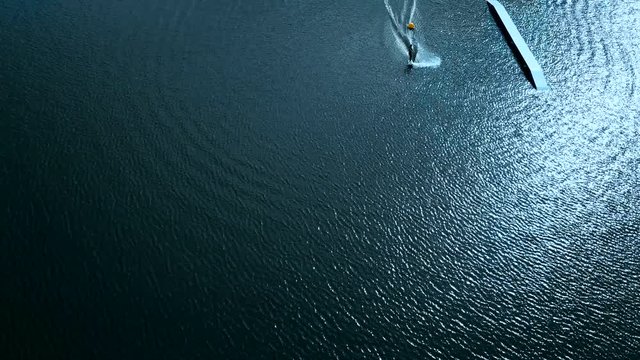 OVERHEAD aerial drone shot of female wake boarding in a cable wakepark on a lake. 4K UHD 60 FPS 