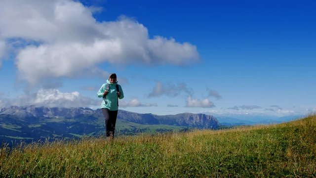 Tourist climbs the green slope agains a backdrop of mountains and blue sky