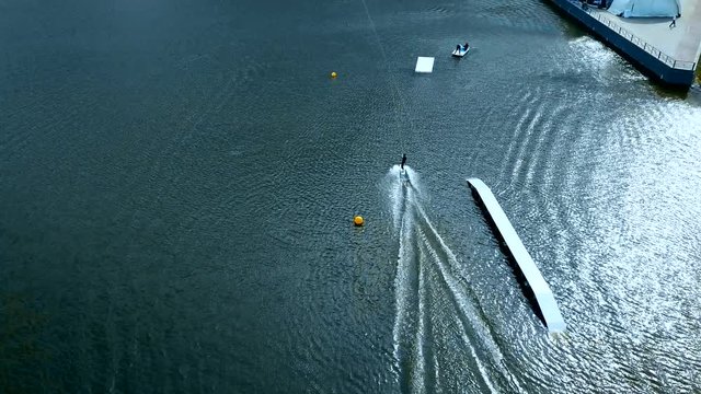 OVERHEAD aerial drone shot of female wake boarding in a cable wakepark on a lake. 4K UHD 60 FPS 
