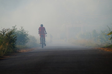 Young boy riding through the smoke on a rough road. Small village in Goa, India.