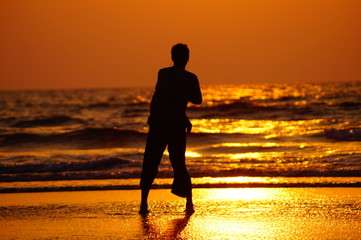 Young guy dancing on the beach during sunset, silhouette of a man