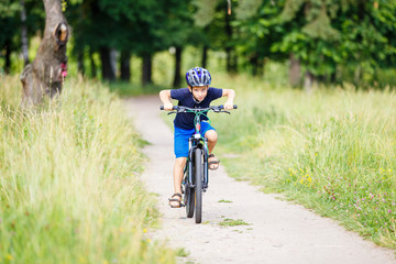 Small boy in protective helmet riding bicycle in park on summer day