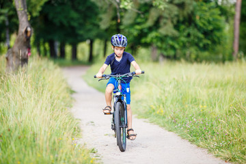 Small boy in protective helmet riding bicycle in park on summer day