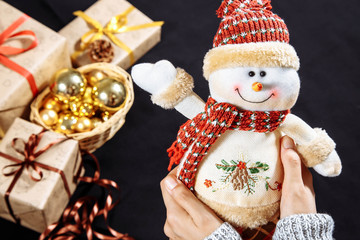 Closeup of a snowman in female hands on a background of Christmas gifts and decorations.