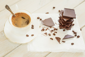Pieces of chocolate with a cup of coffee presented on a white napkin decorated with loose coffee beans