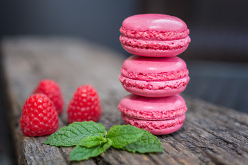 Fototapeta na wymiar Delicious macarons raspberry flavored with fresh raspberries and a sprig of mint presented on a wooden shelf