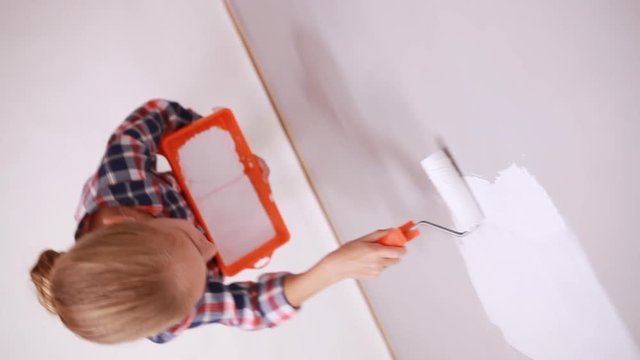 Girl 9 years old repairing her house using paint roller and white color. Top view