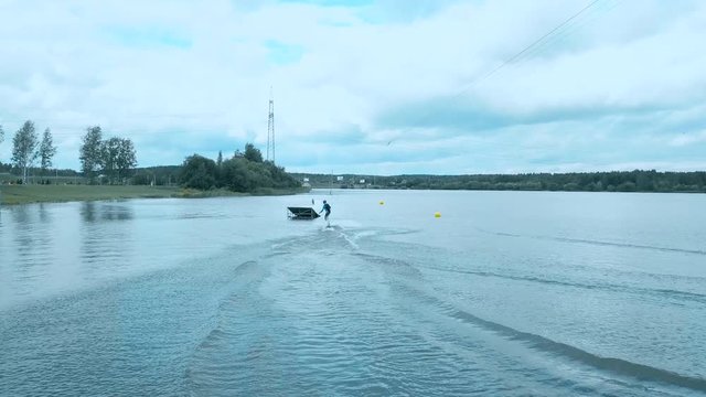 Attractive female practicing wakeboarding tricks in a wakepark near a city. 4K UHD 60 FPS 