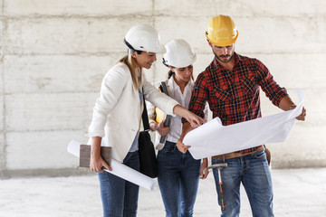 Team of  inspectors and architects discuss about blueprints on construction site.