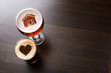 Loving local craft beer. House and heart silhouettes in two glasses of fresh beer on pub table, view from above