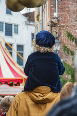 Obraz na płótnie Canvas Nice little boy with blond curls sitting on the shoulder of his father during the Dickens Festival
