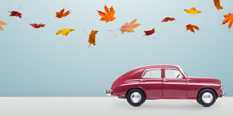 Autumn red toy car with fallen leaves against minimalistic blue background