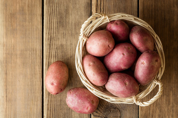 Raw potatoes in basket on wooden background