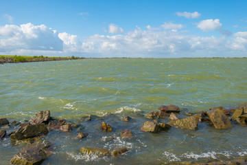 Dike along the shore of a stormy lake in sunlight in summer
