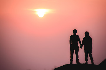 Silhouette of romantic couple standing, holding hands and watching beautiful sunrise in morning. Romance and love concept.