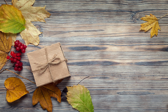 cardboard box tied with string on a bow on a wooden background in autumn leaves, holiday gift on Thanksgiving Hellouin. view from the top. copy space