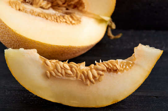 Fresh sweet yellow melon sliced on wooden black table. A piece of raw organic melon on wooden dark surface close up