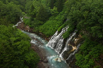 Fototapeta na wymiar Beautiful Shirogane Falls dropping into a blue river, Biei, Hokkaido, Japan