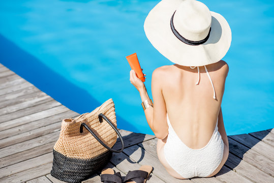 Woman in sunhat sitting with sunscreen lotion near the basin with blue water. Sunscreen solar cream uv protection concept
