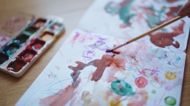 Hands of little girls painting with watercolors in album on the floor.