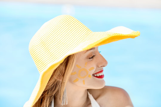 Close-up portrait of a young woman in yellow hat with sun painting on her cheek on the blue water background