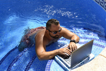 Hombre con laptop esta en la piscina disfrutando el verano