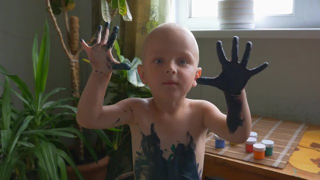 Funny little boy all dirty showing hands in paint