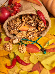 Nuts in a sack, fruits and vegetables on fallen leaves background, autumn season