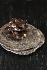 Pieces of black chocolate lie on a dark plate that stands on a black background.