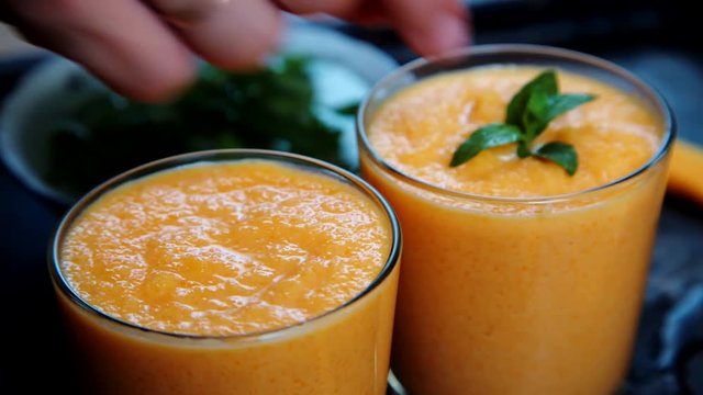Close-up shot of person decorates orange smoothie with leaves of fresh mint