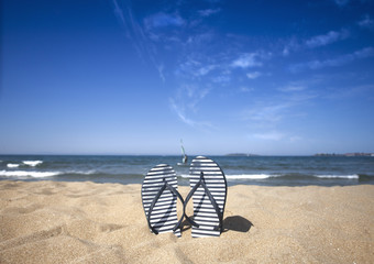 Blue sandal flip flop on the sand beach with blue sea and sky background in summer vacations. Copy...