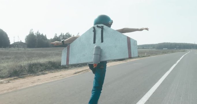 TRACKING Little boy wearing helmet and styrofoam wings running on a rural road, pretending to be a pilot. 4K UHD RAW edited footage