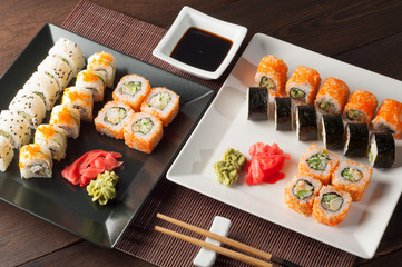 Sushi rolls on a black and white plate, on a wooden mat with chopsticks and soy sauce
