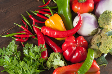 Harvest of different peppers and vegetables on a wooden background