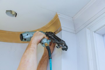 Carpenter brad using nail gun to Crown Moulding framing trim, with the warning label that all power...