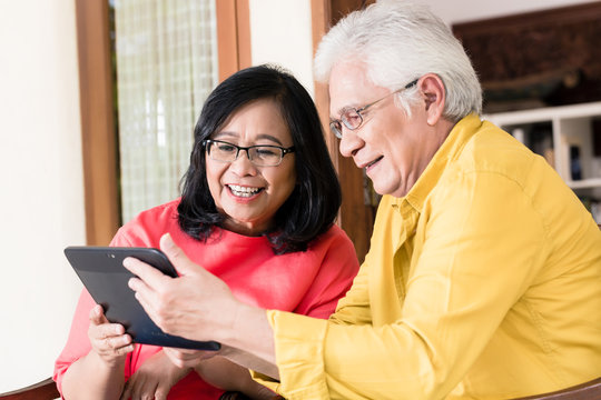 Asian senior couple in love smiling while holding tablet computer