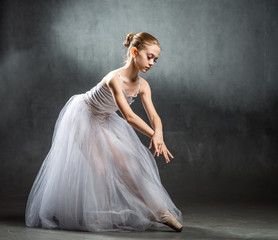 Beautiful young ballerina is dancing in the studio on a dark background. A little dancer. Ballet dancer.