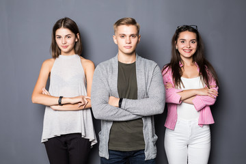 Happy young friends standing indoors on gray background